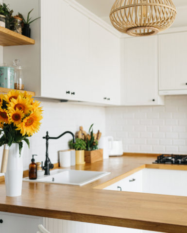 View on clean white simple modern kitchen in scandinavian style, kitchen details, wooden table, sunflowers bouquet in vase on the table